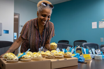 A middle-aged African-American woman celebrates a product milestone with cupcakes and team awards, creating a festive atmosphere and reinforcing a culture of appreciation and gratitude