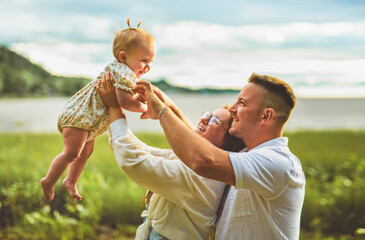 family with baby child girl at the sunset on the waterscape view from back