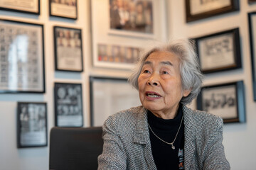 An elderly Asian woman recites motivational quotes from a framed collection, inspiring interns with timeless wisdom and perseverance stories.