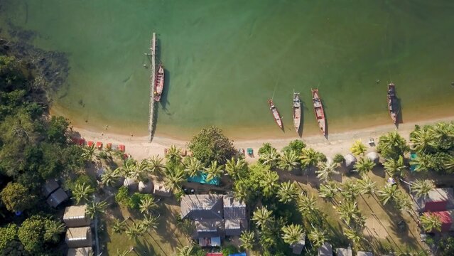 Koh Tonsay offers stunning aerial views with boats anchored along the sandy shore, surrounded by lush palm trees and vibrant beach sets at sunrise.