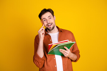Handsome man in casual orange shirt holding colorful notebooks and pencil, smiling confidently...