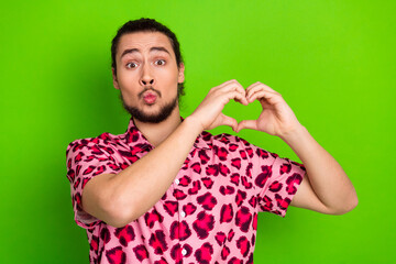 Young man in a pink leopard-printed shirt making a heart shape with hands on a bright green...