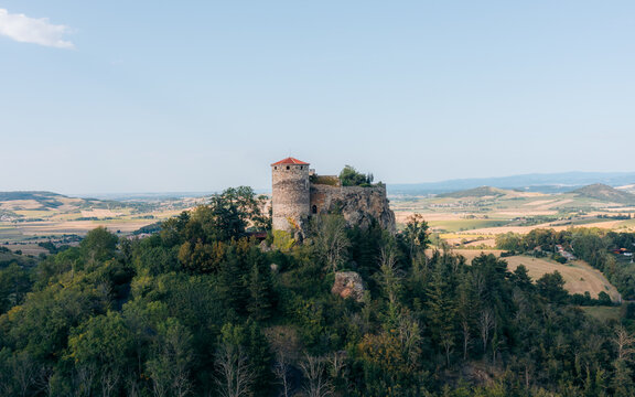 Aerial view of the ancient Ch&Atilde;&cent;teau de Buss&Atilde;&copy;ol perched atop a verdant hill, its weathered stone tower contrasting against the soft blue sky, Buss&Atilde;&copy;ol, Auvergne-Rh&Atilde;&acute;ne-Alpes, France.