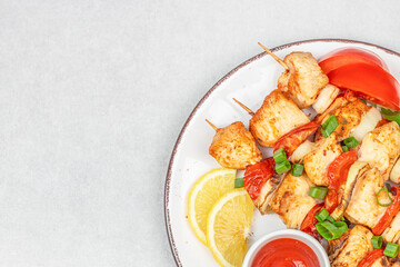 Grilled chicken skewers with vegetables, lemon slices, and dipping sauce served on a white plate. copy space, top view