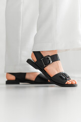 A woman is dressed in stylish white pants paired with black sandals