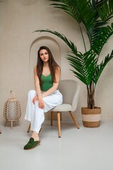 A woman is comfortably seated in a stylish chair, positioned next to a lovely potted plant, which adds a touch of nature to the scene
