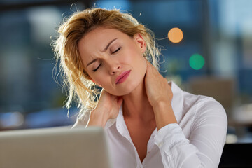 Woman sitting at desk, holding her neck in discomfort while working on a laptop