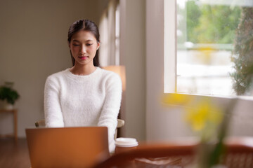 Young Asian woman remote worker using laptop computer working from home modern cozy office space...