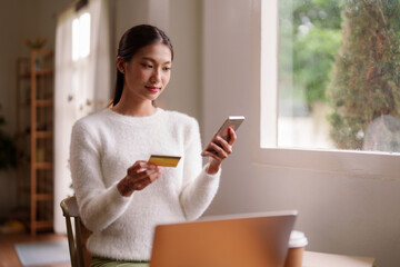 Asian adult woman online shopping from home conveniently using mobile banking and credit card for...