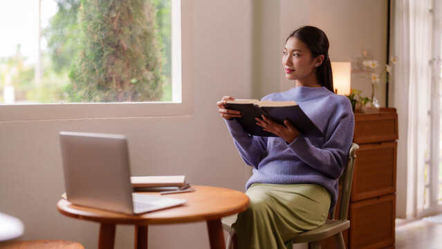 Asian young adult woman reads book at home by window tranquil indoor setting enjoying peaceful moments wellbeing modern lifestyle - Powered by Adobe