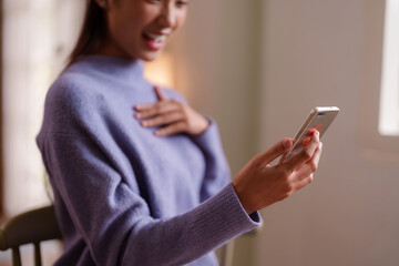 Asian young adult woman enjoys mobile content at home comfortable cozy setting happy surprise engaging digital communication internet browsing leisure lifestyle