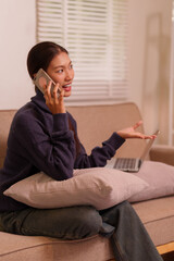 Asian adult woman remote working home office communicating on mobile phone multitasking with laptop for virtual meeting
