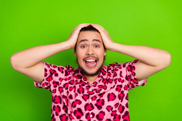 Excited young man in a vibrant printed shirt expressing surprise against a vivid green background,...