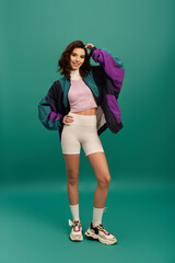 Stylish young woman showcases trendy sporty outfit against turquoise backdrop