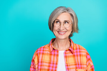 Smiling elderly woman wearing stylish checkered shirt against teal background, exuding charm,...