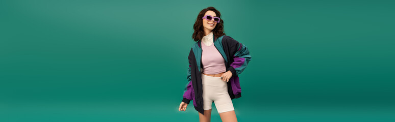 Trendy young woman showcases sporty fashion on vibrant turquoise backdrop