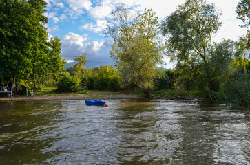 Blue Rowboat Floating on a Sunlit Lakeshore with Trees and Clouds