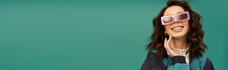 Stylish young woman poses playfully in sporty outfit on vibrant turquoise backdrop