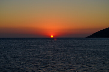 The ocean is calm and the sky is a beautiful orange color. The sun is setting, creating a warm and...