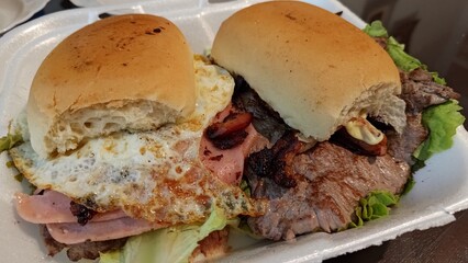 Close up of Chivito, a tradicional uruguayan steak sandwich with fried egg, ham, bacon, and lettuce...