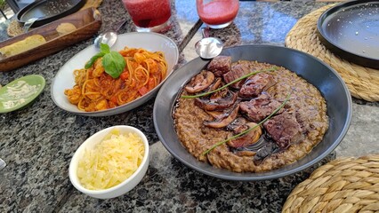 Delicious gourmet lunch with beef and mushroom risotto and shrimp spaghetti on a restaurant table. Includes grated cheese, bread, and red fruit smoothies for a complete dining experience.