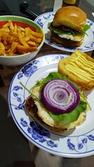 Close up of two homemade beef burgers with fried egg, spinach, and red onion on brioche buns, served with a side of seasoned french fries in a bowl on a dark table. Casual fast food meal.