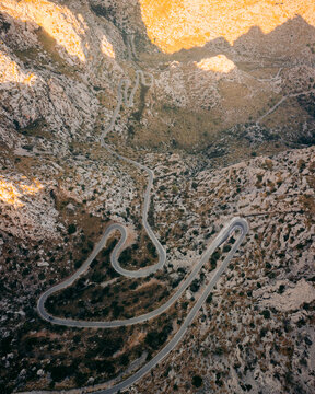Aerial view of a winding mountain road snaking through the rugged, sun-drenched landscape of Nus de sa Corbata, Escorca, Mallorca, Spain.