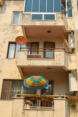 Brightly colored umbrella and satellite dishes adorn a balcony in a residential building during...