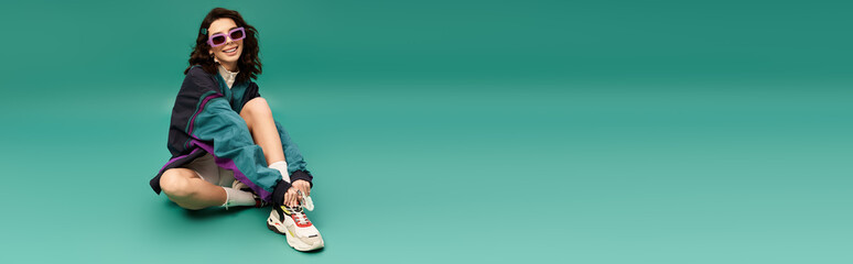 Obraz premium Young woman in fashionable sporty attire relaxes on the floor with a playful smile