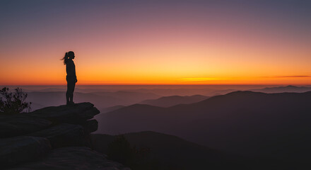 Silhouette of a woman admiring sunset over mountain ranges at dusk