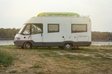 Side view of white camper van parked on grassy Danube riverbank, roof loaded with bright green kayak under warm evening light, symbolizing outdoor travel freedom and vanlife adventure.