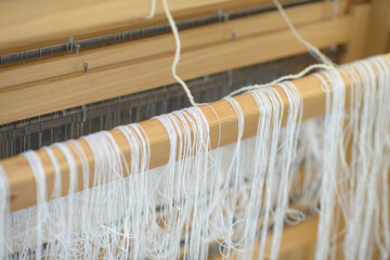 Wooden handloom as fine white warp threads drape over the beam, highlighting traditional textile craft, precise setup, and the slow art of fabric making.