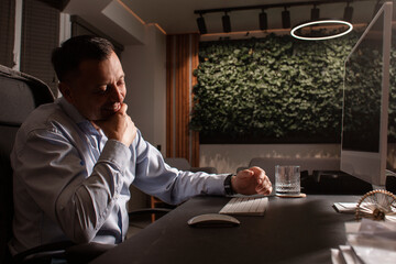 Smiling middle-aged businessman relaxing at his desk in a modern eco-friendly office. Warm...