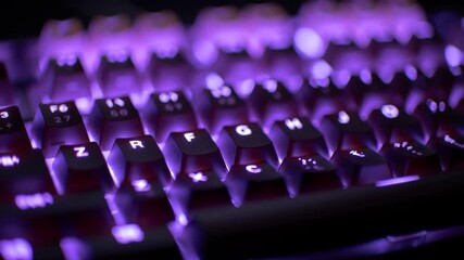 Illuminated keys on a dark keyboard glow purple. Keys are slightly blurry, some showing letters and numbers. Background is dark and out of focus, also showing the purple lighting - Powered by Adobe