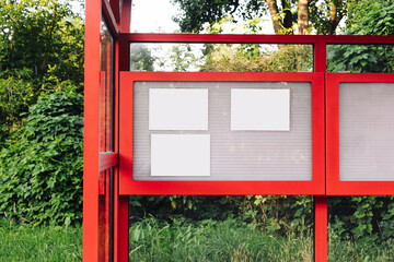 Public message board on red bus stop. Blank white notes on display case. Outdoor urban announcement...