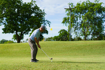 Elderly Asian man enjoying the morning round of golf in soft and warm sunlight.
