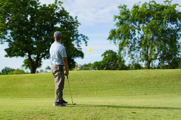 Elderly Asian man enjoying the morning round of golf in soft and warm sunlight.