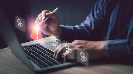 Businessman using digital pen and laptop, detecting system error with warning icon. Concept for issue detection, troubleshooting, and problem-solving in modern technology.