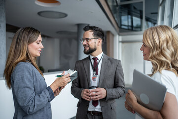 Businesswoman taking notes while talking to colleagues in office hallway
