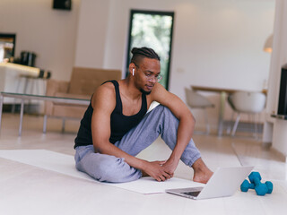 Training At Home. Sporty man doing the training while watching an online tutorial on a laptop, exercising in the living room, free space.