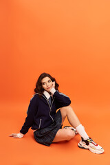 Stylish young woman showcasing contemporary fashion against vibrant orange backdrop