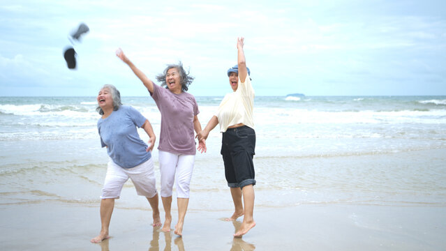 Happy senior women enjoying a playful walk on the beach, - Powered by Adobe