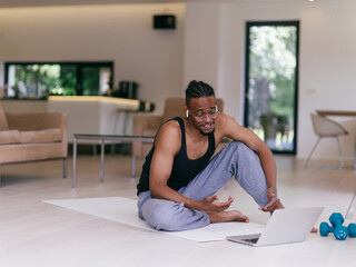 Training At Home. Sporty man doing the training while watching an online tutorial on a laptop, exercising in the living room, free space.