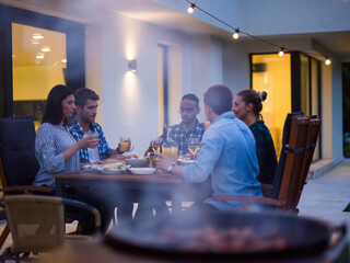 A group of young diverse people having dinner on the terrace of a modern house in the evening. Fun for friends and family. Celebration of holidays, weddings with barbecue