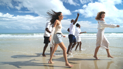 Group of diverse friends having fun at the beach, walking and splashing in the waves