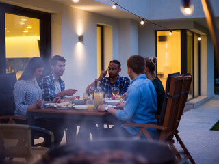 A group of young diverse people having dinner on the terrace of a modern house in the evening. Fun for friends and family. Celebration of holidays, weddings with barbecue