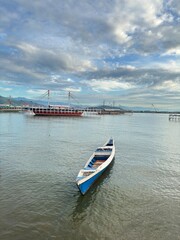 Fototapeta premium Serene blue and white rowboat floats on calm water with a large passenger ship sailing in the distance under a dramatic cloudy sky