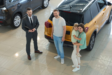 Salesman with clipboard showing new car to happy family in salon