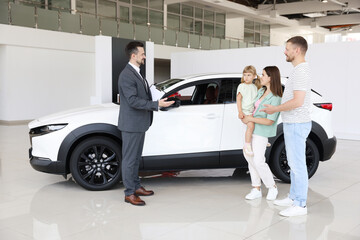 Smiling salesman with clipboard showing new car to family in salon