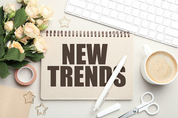 New Trends inscription in notebook, computer keyboard, flowers, coffee and stationery on beige...